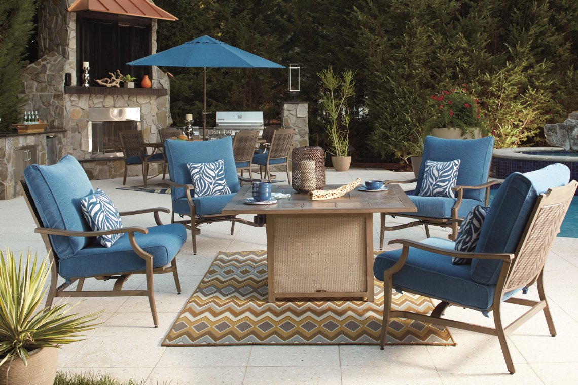 Outdoor dining set with a firepit, chairs and an outdoor kitchen in the background.