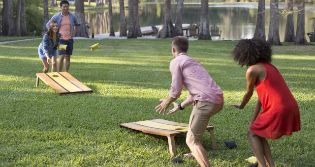 A group of kids playing corn hole in the backyard.