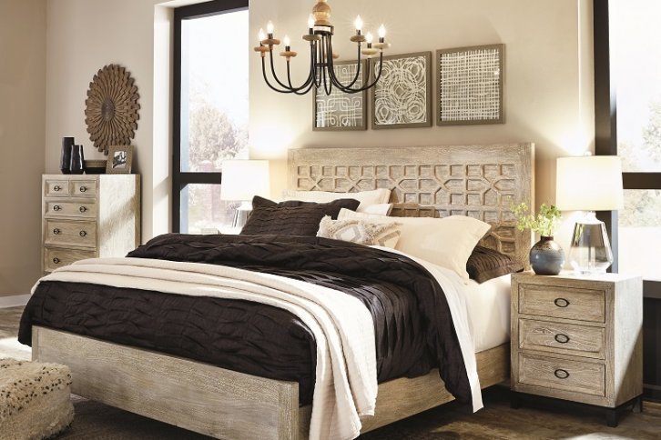 Large bedroom with cream colored wood with a chandelier hanging high above the bed and a nightstand with a lamp next to the bed.