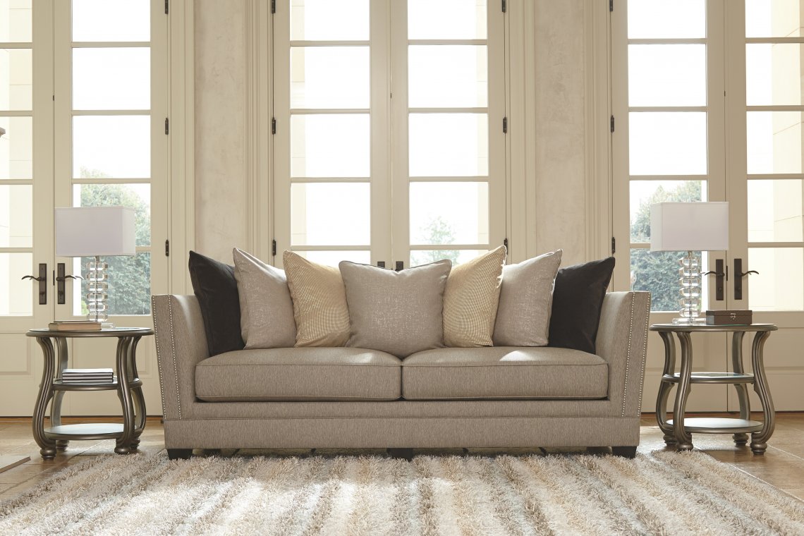 Cream colored sofa with layers of pastel colored pillows with a striped fluffy rug in front.