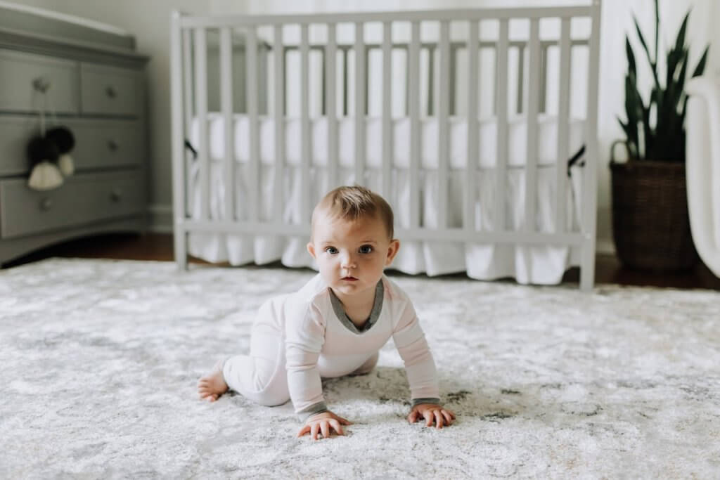 baby on floor next to crib